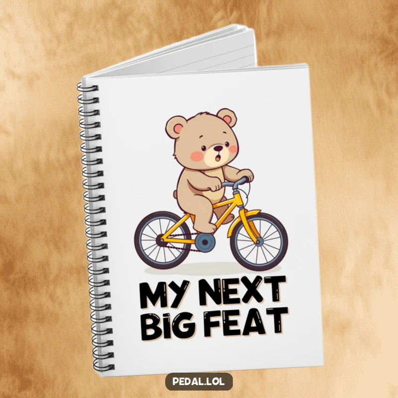 Funny bear pedaling a yellow bicycle uphill with effort, inspiring focus in this humorous notebook.